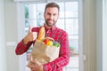 Handsome man holding groceries bag happy with big smile doing ok sign, thumb up with fingers, excellent sign Royalty Free Stock Photo