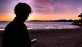 Handsome man holding mobile phone in his hand and texting message, on sunset background. Colorful sunset over the sea Royalty Free Stock Photo