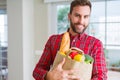 Handsome man holding paper bag full of fresh groceries at home Royalty Free Stock Photo