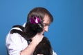 Handsome man holding on sholder black cat in pink shiny crown on blue background with copy space