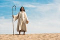 Man in jesus robe holding wooden cane against blue sky in desert