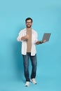 Handsome man with laptop showing thumb up gesture on light blue background Royalty Free Stock Photo