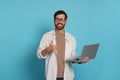 Man with laptop showing thumb up gesture on light blue background Royalty Free Stock Photo