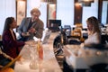 Handsome man leaned on a bar, talking female bartender, smiling, in company of young woman