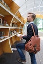 Handsome man with leather backpack choosing book on bookcrossing station in the park. Student in free street library book exchange