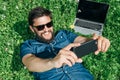 Handsome man lying on green grass in the park and listening music