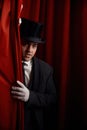 Handsome man magician peeking out from behind stage drapery curtain Royalty Free Stock Photo