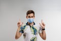 Handsome man in medical mask points up. Quarantine covid-19 period. Man weared t-shirt isolated white background Royalty Free Stock Photo