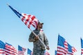 Man in military uniform and cap holding american flag while standing against blue sky Royalty Free Stock Photo