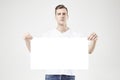 Handsome man model standing with blank big poster or sheet in hands, isolated on white background, wearing jeans and t-shirt. Royalty Free Stock Photo