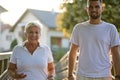 A handsome man and an older woman share a serene walk in nature, crossing a beautiful bridge against the backdrop of a Royalty Free Stock Photo