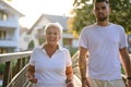 A handsome man and an older woman share a serene walk in nature, crossing a beautiful bridge against the backdrop of a Royalty Free Stock Photo