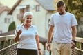 A handsome man and an older woman share a serene walk in nature, crossing a beautiful bridge against the backdrop of a Royalty Free Stock Photo