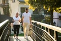 A handsome man and an older woman share a serene walk in nature, crossing a beautiful bridge against the backdrop of a Royalty Free Stock Photo