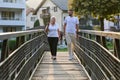 A handsome man and an older woman share a serene walk in nature, crossing a beautiful bridge against the backdrop of a Royalty Free Stock Photo