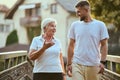 A handsome man and an older woman share a serene walk in nature, crossing a beautiful bridge against the backdrop of a Royalty Free Stock Photo