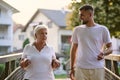 A handsome man and an older woman share a serene walk in nature, crossing a beautiful bridge against the backdrop of a Royalty Free Stock Photo