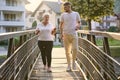 A handsome man and an older woman share a serene walk in nature, crossing a beautiful bridge against the backdrop of a Royalty Free Stock Photo