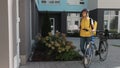 Handsome man open door to a pizza delivery woman wearing yellow thermal backpack on a bike and recieves cardboard boxes Royalty Free Stock Photo