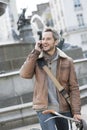 Handsome man at phone on a bicycle with fountain in background