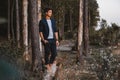 Handsome man posing outdoors in forest stands barefoot on a log, wearing checked jacket. Place for text or advertising Royalty Free Stock Photo