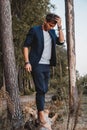 Handsome man posing outdoors in forest stands barefoot on a log, wearing checked jacket. Place for text or advertising Royalty Free Stock Photo