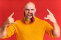 handsome man with raindow in beard and yellow sweater in red studio baclground