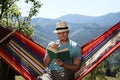 Handsome man reading book in hammock outdoors on sunny day Royalty Free Stock Photo