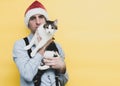 Man in red christmas santa hat, blue shirt and black suspender holding cute white with brown tabby cat and looking at camera Royalty Free Stock Photo