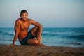 Handsome man on a sandy beach sits on the seashore. Young man on the coast