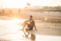 Handsome man on a sandy beach sits on the seashore. Young man on the coast