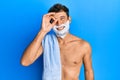 Handsome man saving beard with shave foam over face smiling happy doing ok sign with hand on eye looking through fingers