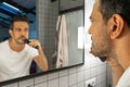 Handsome man is shaving his beard with trimmer machine in front of bathroom mirror Royalty Free Stock Photo