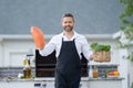 Handsome man in shirt and in cook apron preparing fish on barbecue. Grilling salmon outdoor. Male cook cooking salmon