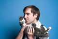 Man in shirt holding and snuggling up cheek to cute gray and white cat muzzle and looking away