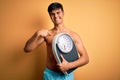 Handsome man shirtless wearing swimwear holding weight machine over yellow background with surprise face pointing finger to Royalty Free Stock Photo