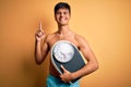 Handsome man shirtless wearing swimwear holding weight machine over yellow background surprised with an idea or question pointing Royalty Free Stock Photo