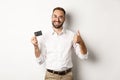 Handsome man showing his credit card and thumb up, recommending bank, standing over white background Royalty Free Stock Photo