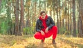 Handsome man sitting posing in the woods at sunrise. A man in a red tracksuit and a black leather jacket Royalty Free Stock Photo