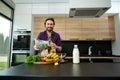 Handsome man smiles looking at camera, holding greens while unpacking eco paper bag with healthy food, standing at kitchen Royalty Free Stock Photo