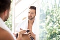 Handsome man standing at bathroom mirror and applying shaving foam Royalty Free Stock Photo