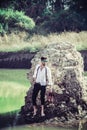 Handsome man standing near rock wearing blue goggle, sun glasses, white shirt, black pant trouser in the lake green water on sunny Royalty Free Stock Photo