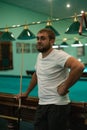 A handsome man stands in the billiard room holding a cue in his hands, leaning on the table and waiting for his turn. A Royalty Free Stock Photo