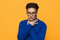 a handsome man stands in black glasses for vision in a blue zip-up jacket, posing on an orange background with his hand