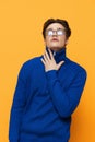 a handsome man stands in black glasses for vision in a blue zip-up jacket, posing on an orange background with his hand