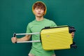 a handsome man stands on a green background, dressed in a yellow panama hat, holding a bright travel suitcase in his Royalty Free Stock Photo