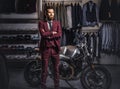 Handsome man with a stylish beard and hair dressed in vintage red suit posing near retro sports motorbike at men`s Royalty Free Stock Photo