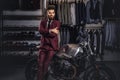 Handsome man with a stylish beard and hair dressed in vintage red suit posing near retro sports motorbike at men`s Royalty Free Stock Photo