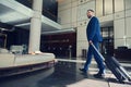 Handsome man, successful business developer smiling, looking to the side, walking down the lobby, heading with luggage to the Royalty Free Stock Photo