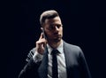 Handsome man in suit talking on mobile phone isolated on dark background Royalty Free Stock Photo